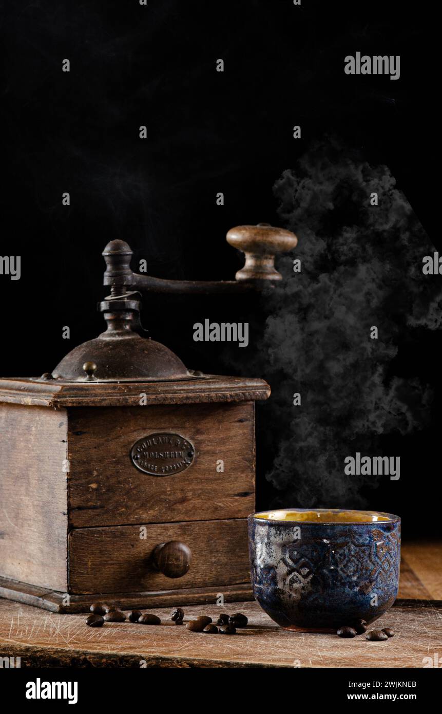 Alte Kaffeemühle mit orientalischer Keramik-Kaffeetasse, auf Holzoberfläche und dunklem Hintergrund Stockfoto
