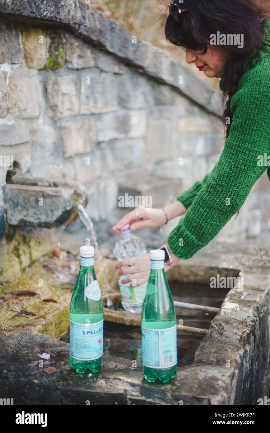 Eine Person in einem grünen Pullover sammelt sauberes Wasser in eine Plastikflasche aus einer natürlichen Quelle, um die Reinheit der Quelle hervorzuheben Stockfoto