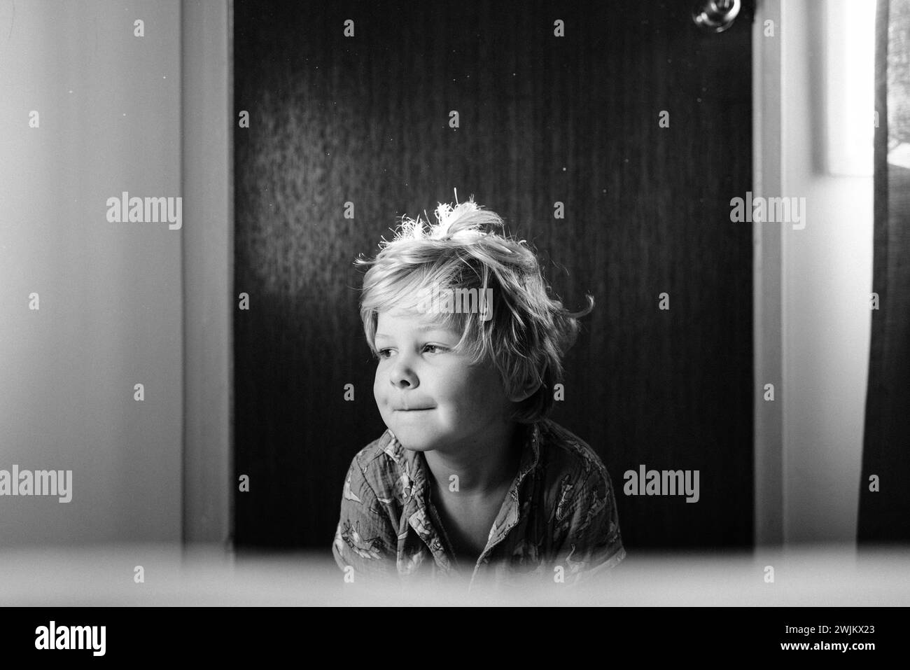 Ein blonder Junge mit einem Lächeln sitzt drinnen in einem Motelzimmer Stockfoto