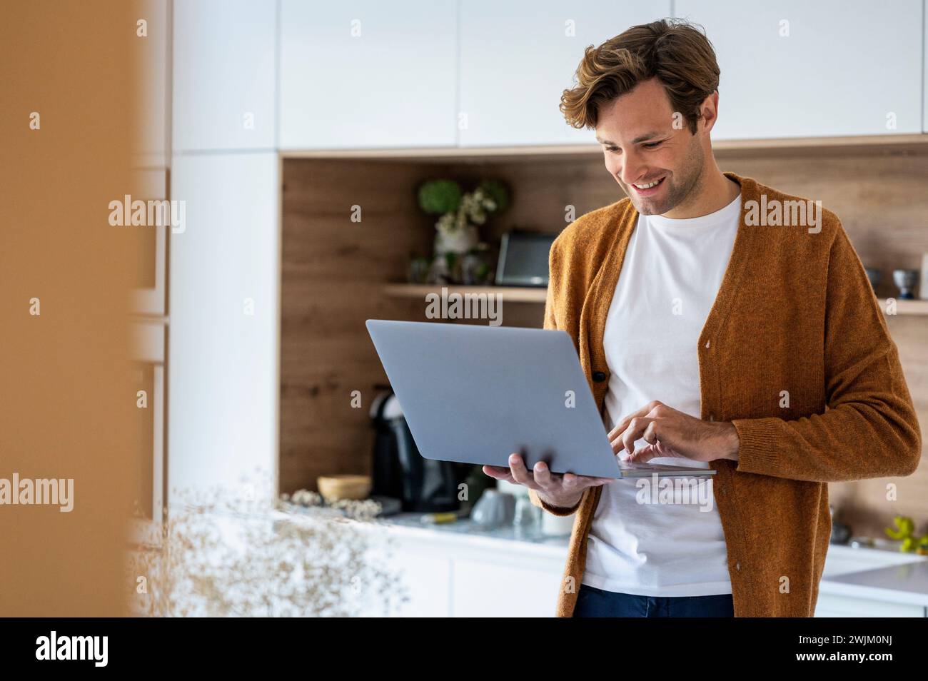 Erwachsener Mann, der in der Küche mit Laptop steht Stockfoto