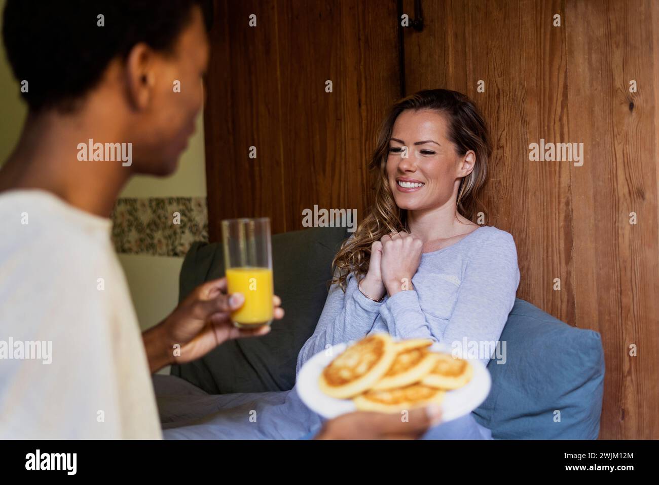 Glückliche Frau, die auf dem Bett lag, während Freunde sie mit Frühstück überraschten Stockfoto