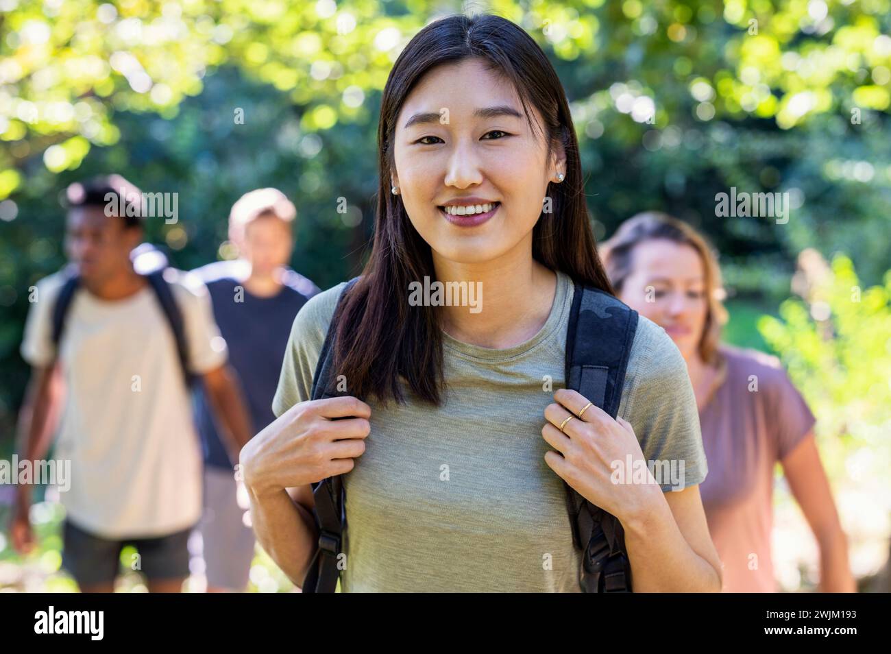Junge Erwachsene Frau, die auf die Kamera blickt, während sie mit Freunden wandert Stockfoto