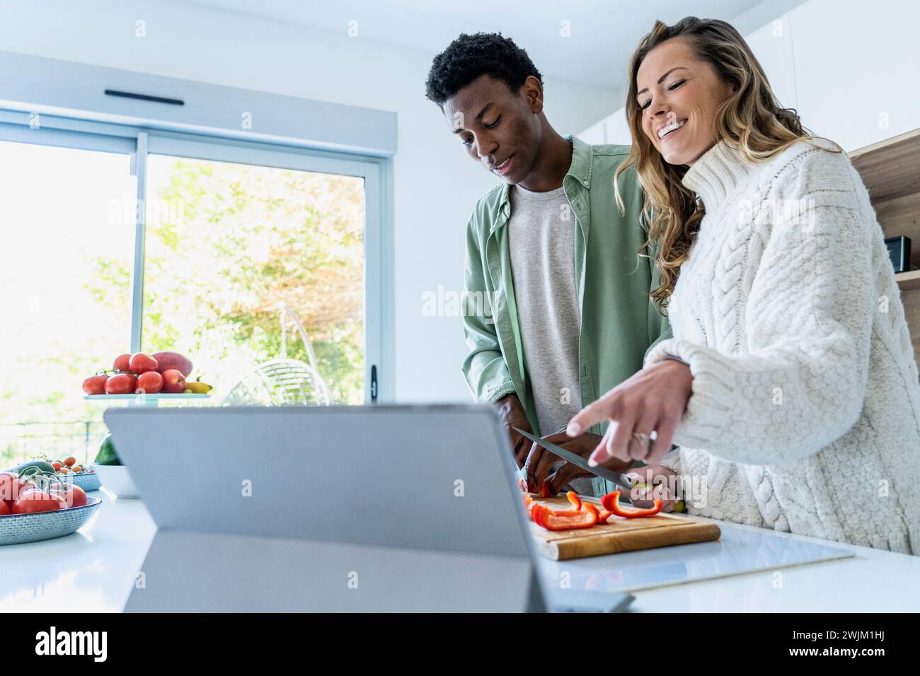 Paare, die sich Kochrezepte auf einem digitalen Tablet ansehen, während sie an der Küchentheke stehen Stockfoto