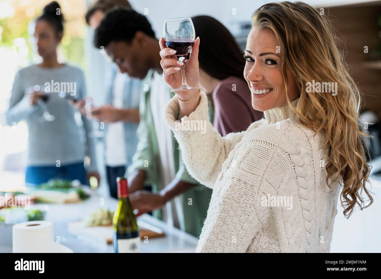 Fröhliche Erwachsene Frau, die auf die Kamera zurückblickt, während sie Weingläser hochhebt Stockfoto