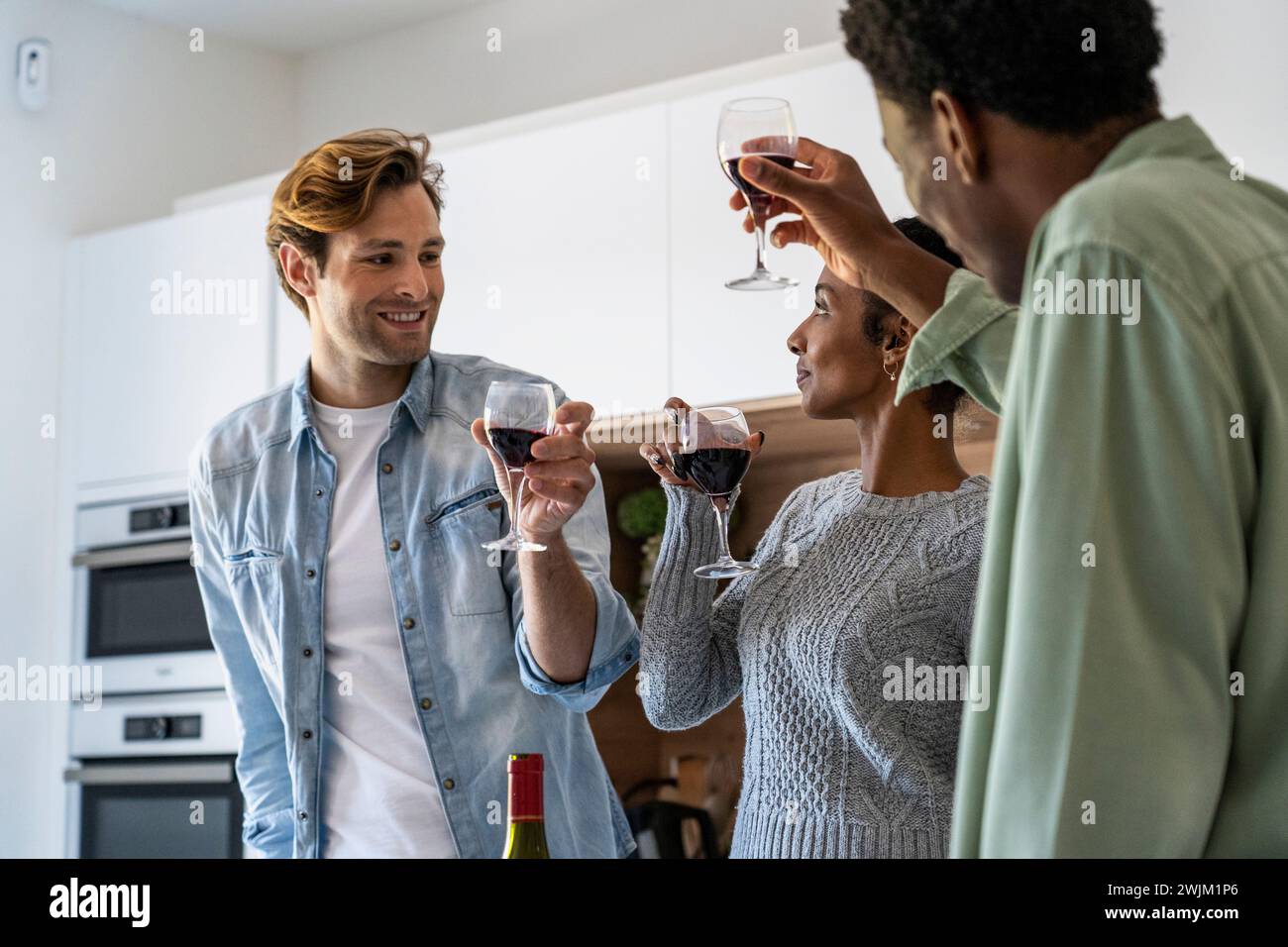 Freunde, die mit Weingläsern beim Wiedersehen in der Küche tosten Stockfoto