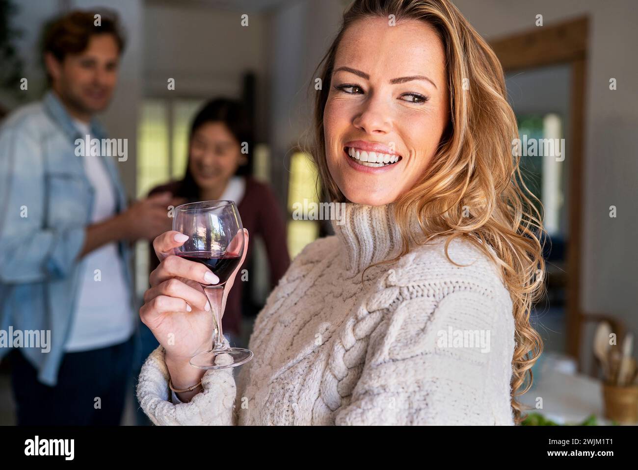 Selbstbewusste Frau, die Weingläser hält, während sie sich mit Freunden auf einer Party versammelt Stockfoto