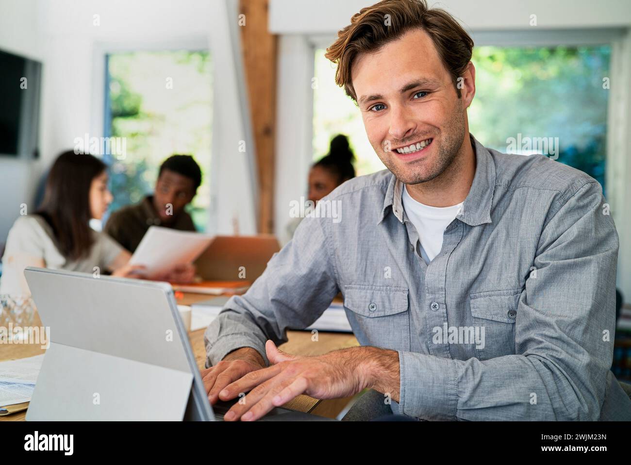 Männlicher Geschäftsadministrator, der während seiner Arbeit am Schreibtisch auf die Kamera schaut Stockfoto