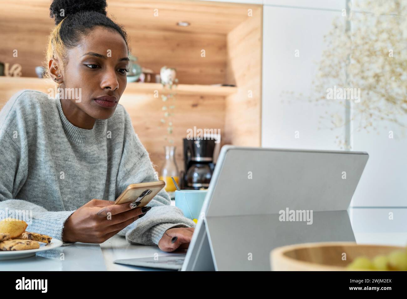 Frau, die ein Smartphone benutzt, während sie an einem digitalen Tablet arbeitet Stockfoto