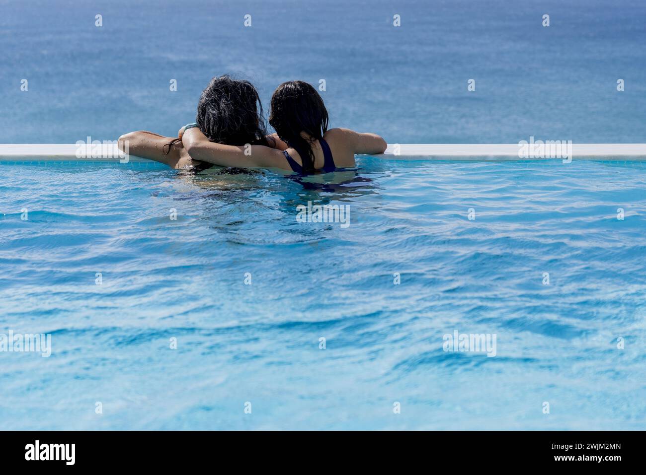 Blick von hinten auf zwei Personen, die sich umarmen, während sie das Meer vom Innenpool aus betrachten Stockfoto