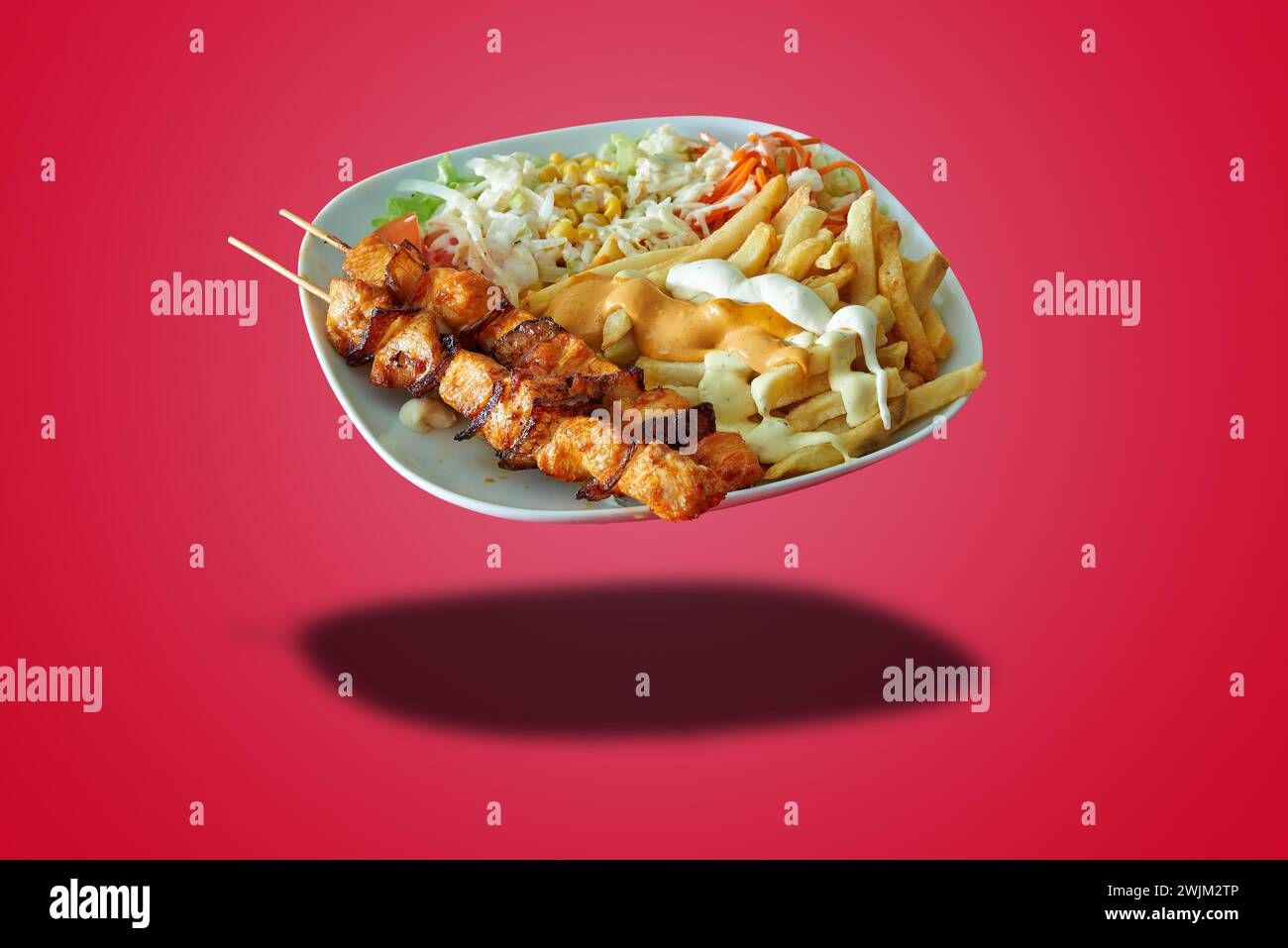 Schwimmender Teller mit Hühnerbroschette und Pommes Frites auf rotem Farbverlauf Stockfoto