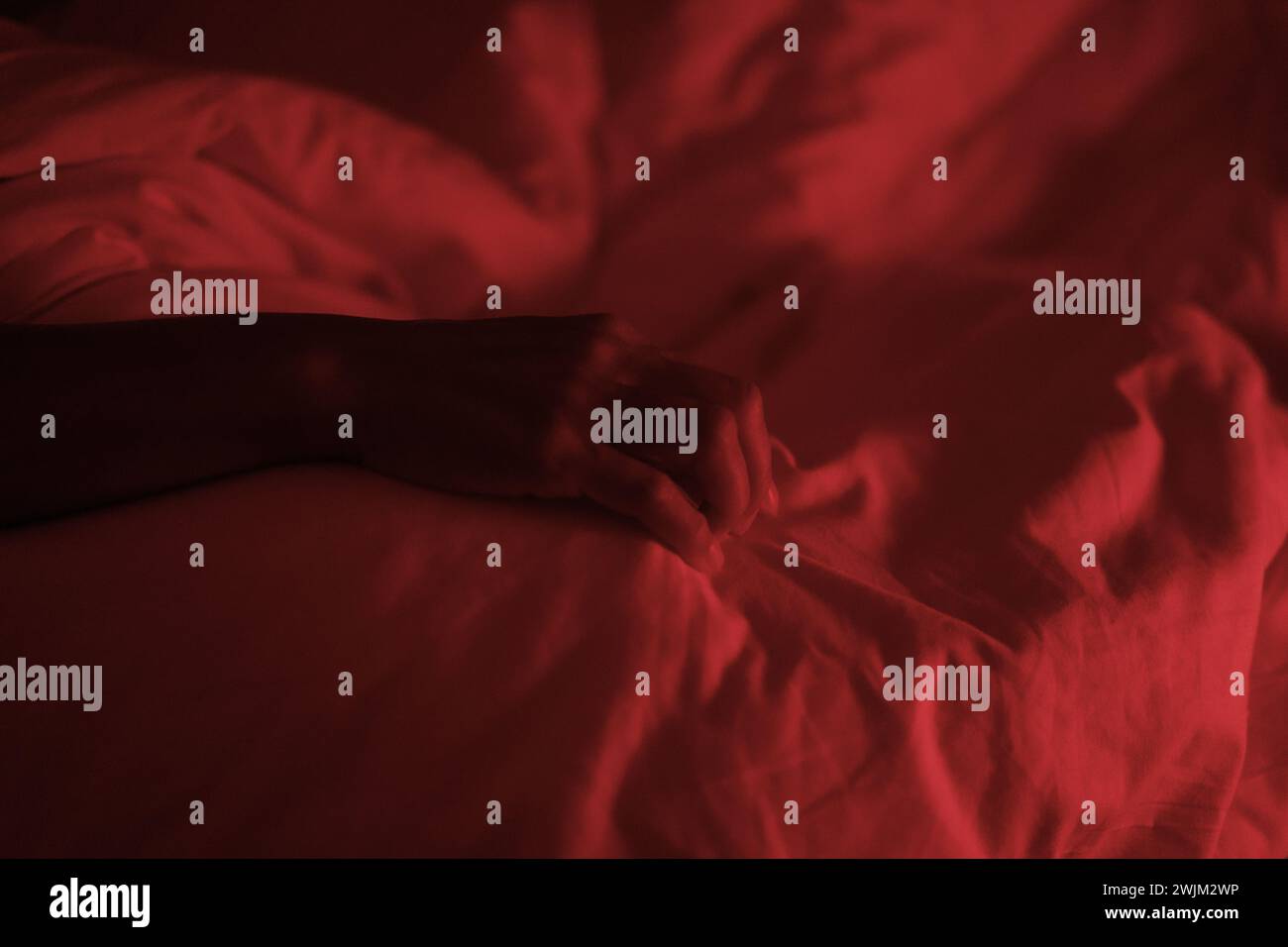 Die Hand der nicht identifizierten Person im Bett unter rotem Licht Stockfoto