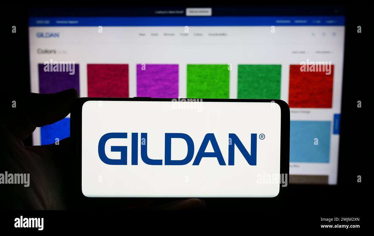 Person mit Smartphone und Logo des kanadischen Bekleidungsunternehmens Gildan activewear Inc. Vor der Website. Schwerpunkt auf dem Display des Telefons. Stockfoto