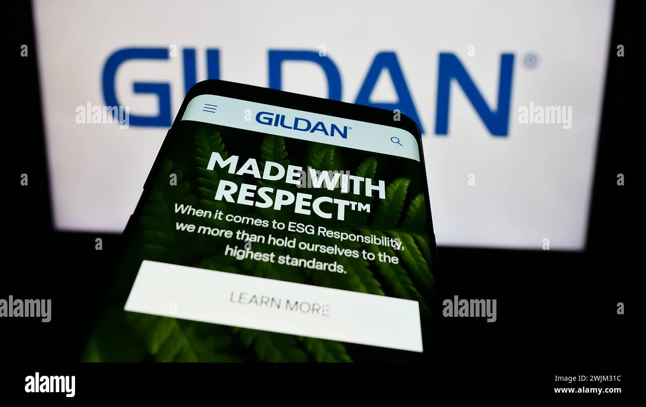 Mobiltelefon mit Website des kanadischen Bekleidungsunternehmens Gildan activewear Inc. Vor dem Geschäftslogo. Fokussieren Sie sich oben links auf der Telefonanzeige. Stockfoto