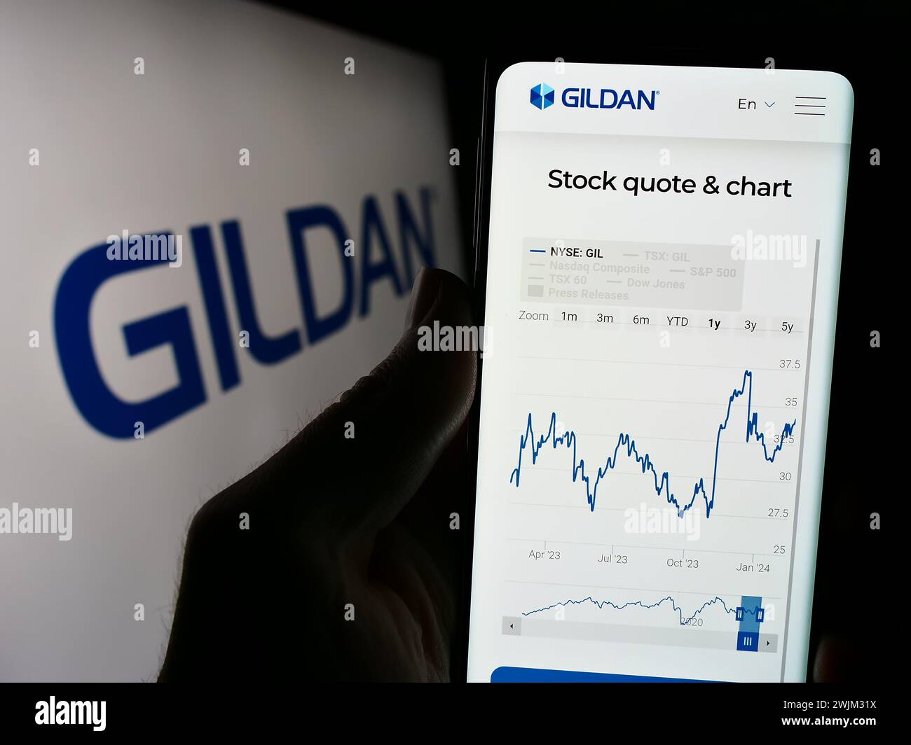 Person mit Smartphone und Webseite des kanadischen Bekleidungsunternehmens Gildan activewear Inc. Vor dem Logo. Konzentrieren Sie sich auf die Mitte des Telefondisplays. Stockfoto