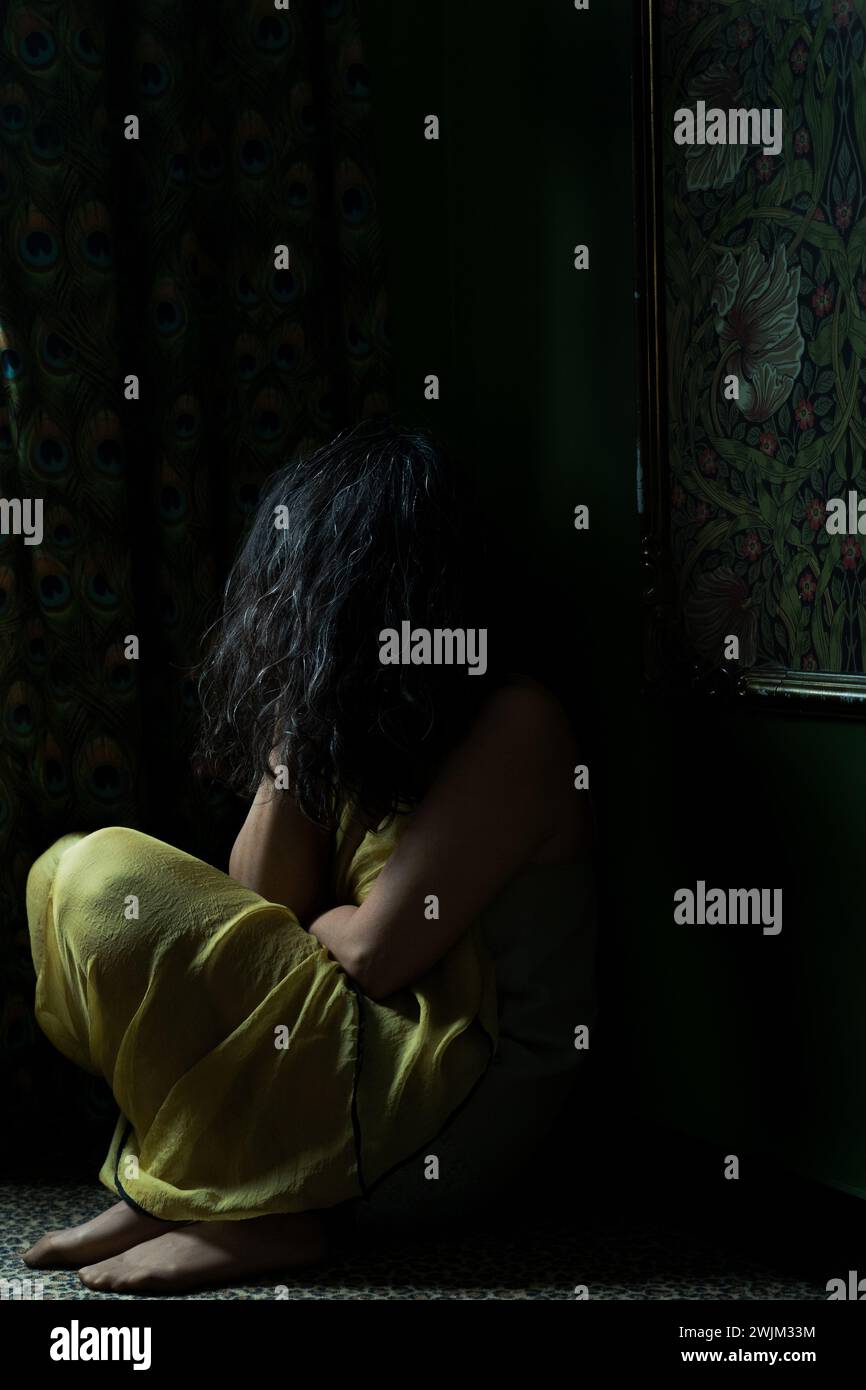 Nicht identifizierte Person, die auf dem Boden in einem dunklen Zimmer sitzt Stockfoto