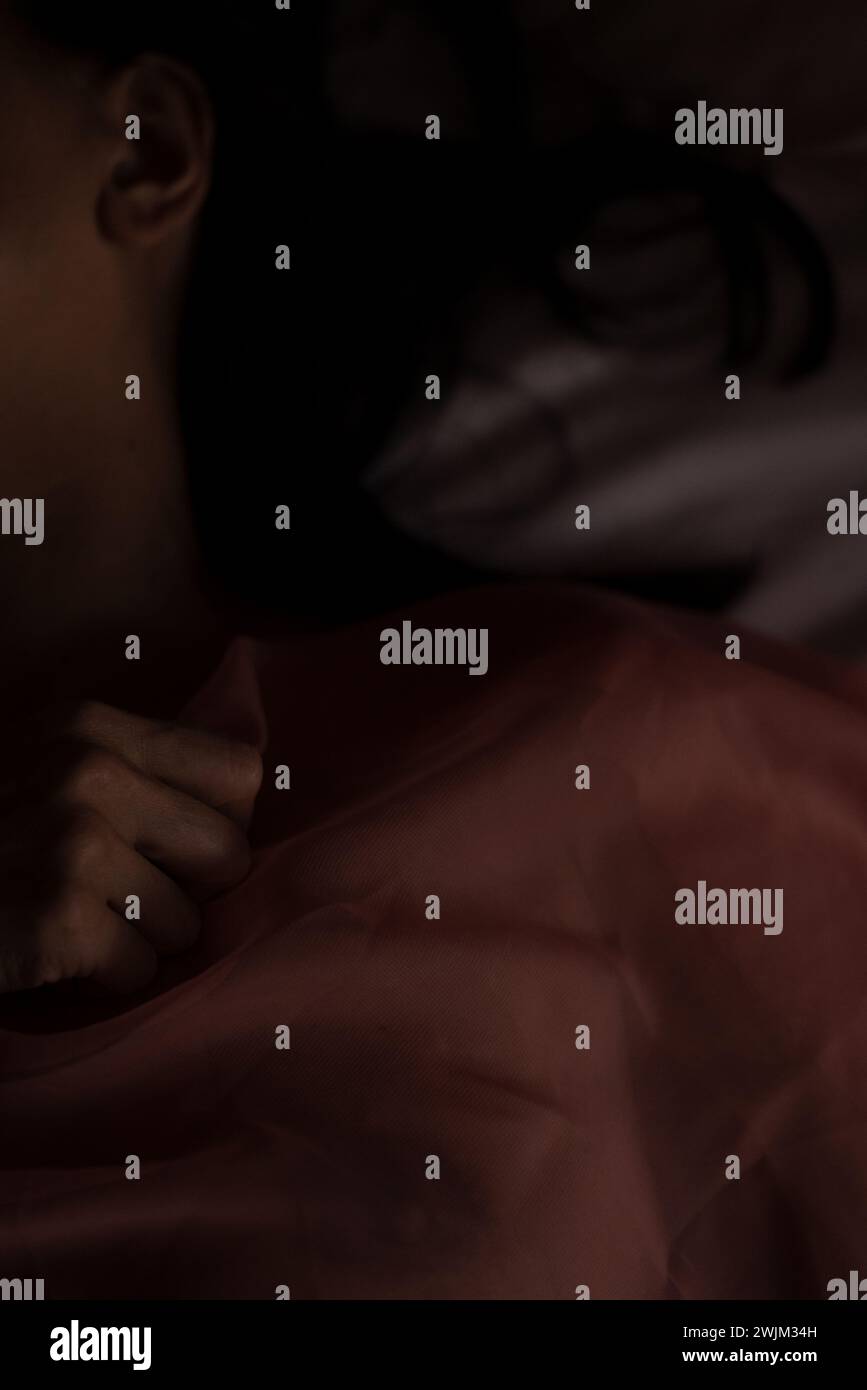 Nicht identifizierte Person, die in einem dunklen Schlafzimmer schläft Stockfoto