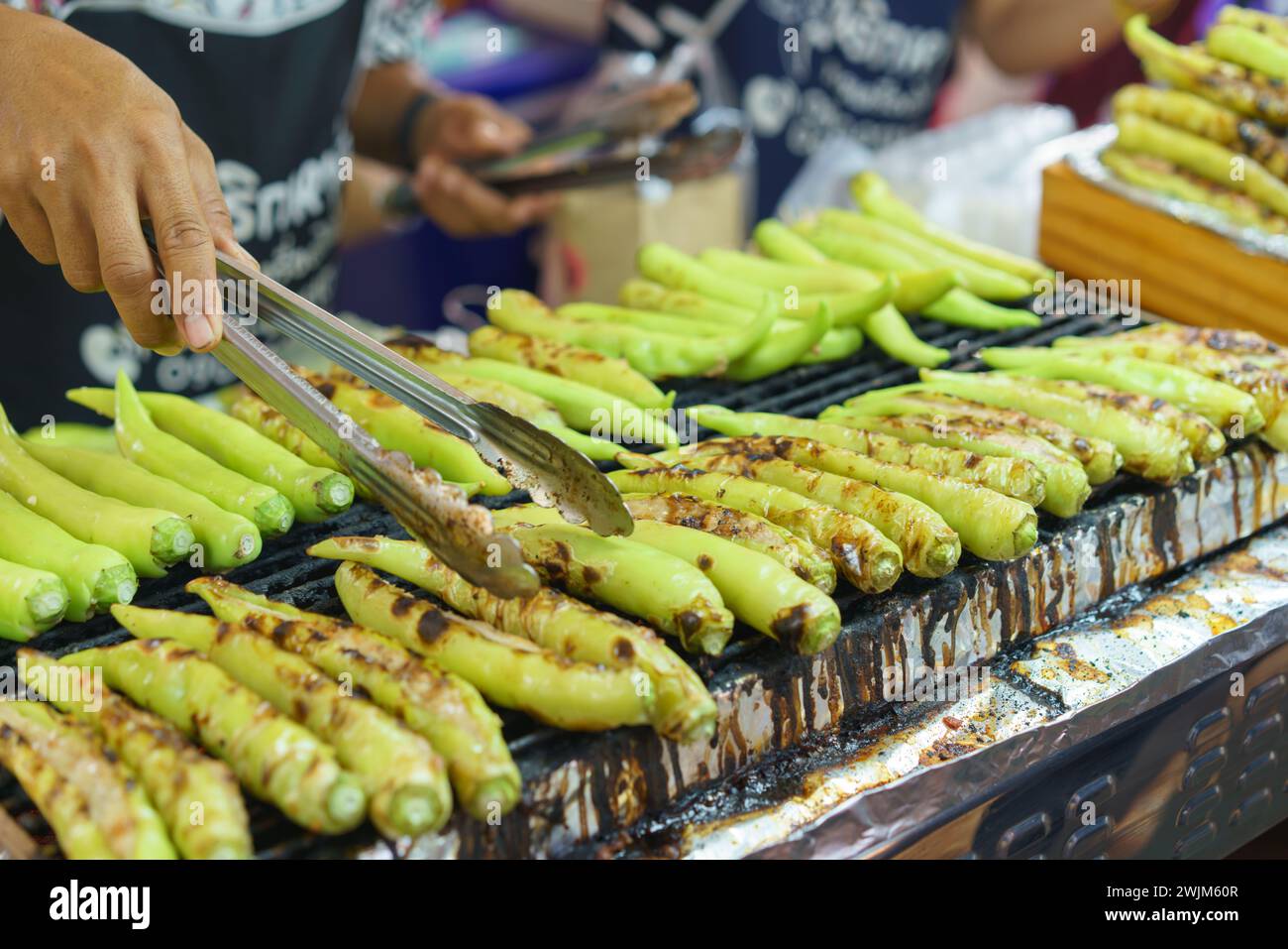 Ein Street Food-Händler grillt fachmännisch eine Menge frischer grüner Chilis, die sie anbraten und als scharfe Beilage serviert werden Stockfoto