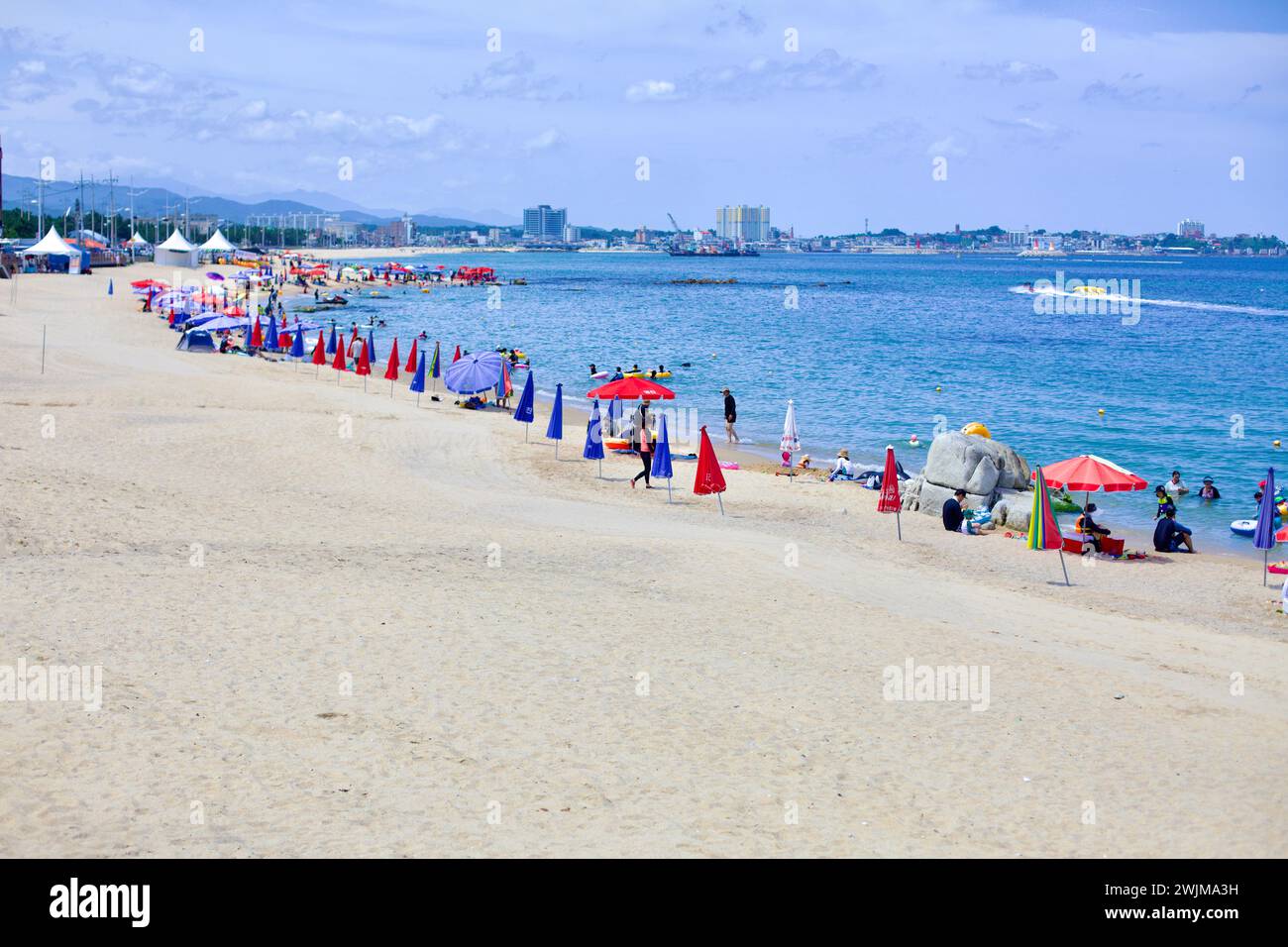 Gangneung City, Südkorea - 29. Juli 2019: Eine lebhafte Szene am Yeongjin Beach mit Booten in der Ostsee, farbenfrohen Sonnenschirmen im Sand und Stockfoto