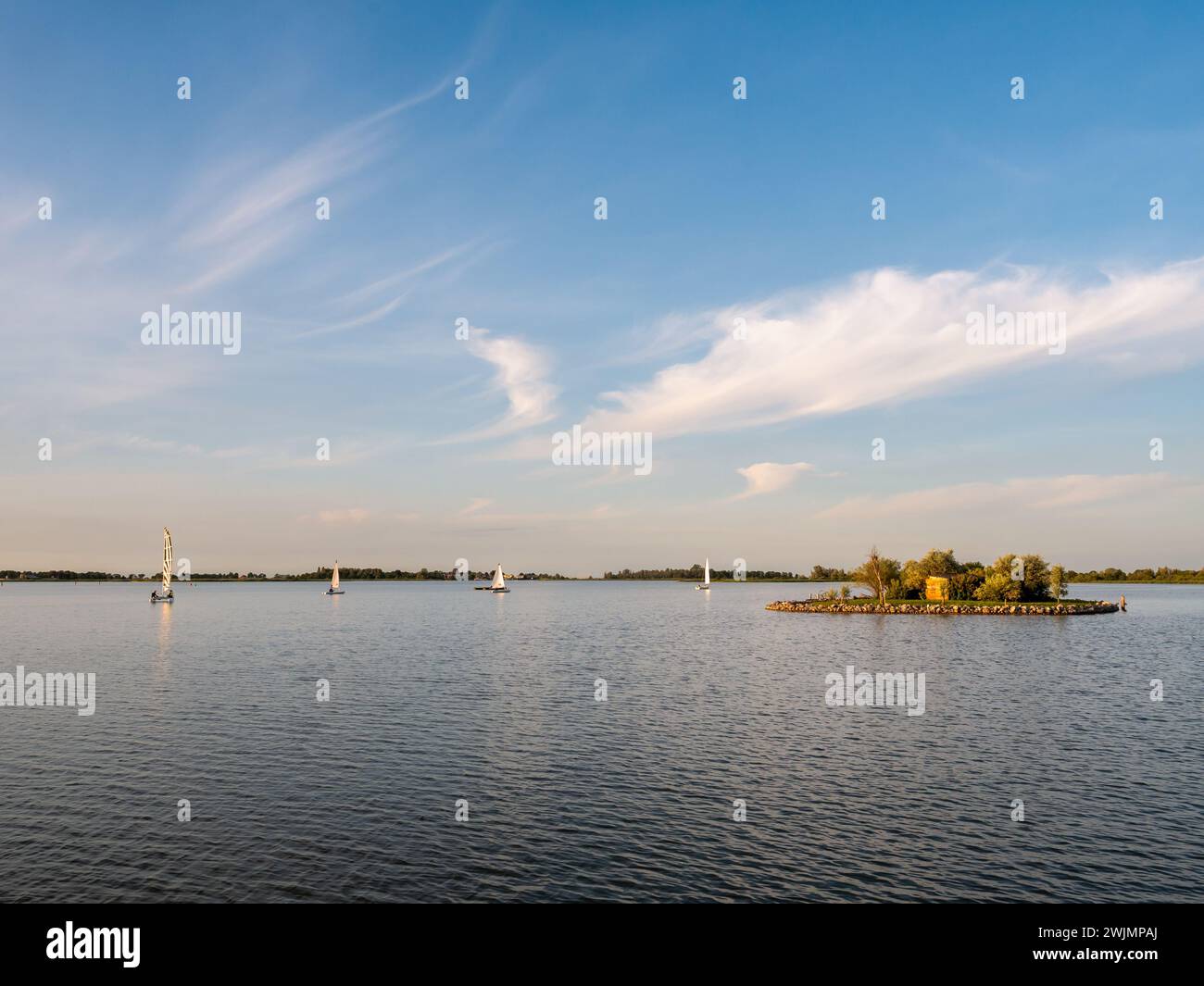 Segelboote umrunden die kleine Insel bei Sonnenuntergang auf dem de Morra See in Friesland, Niederlande Stockfoto