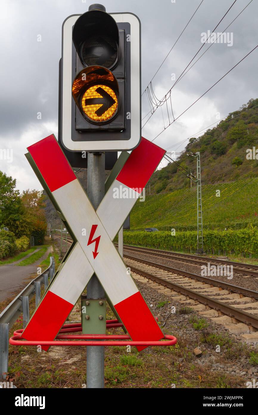 Rot-weißes Verkehrsschild für Bahnübergang mit einem Gelbe Ampel vor einer grünen Landschaft und ein Grauer Himmel Stockfoto