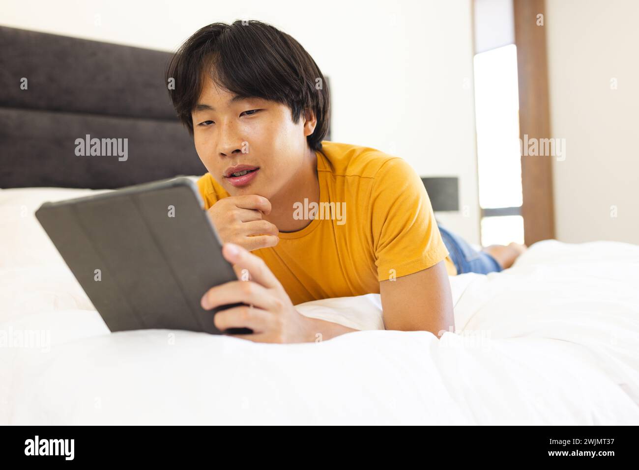 Teenager Asiatischer Junge liegt auf einem Bett mit einem Tablet, mit Kopierraum Stockfoto