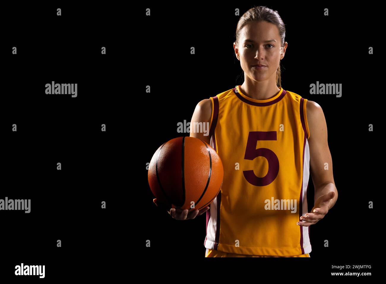 Sportliche Frau in Basketballausrüstung posiert mit Fokus und zeigt Engagement. Stockfoto