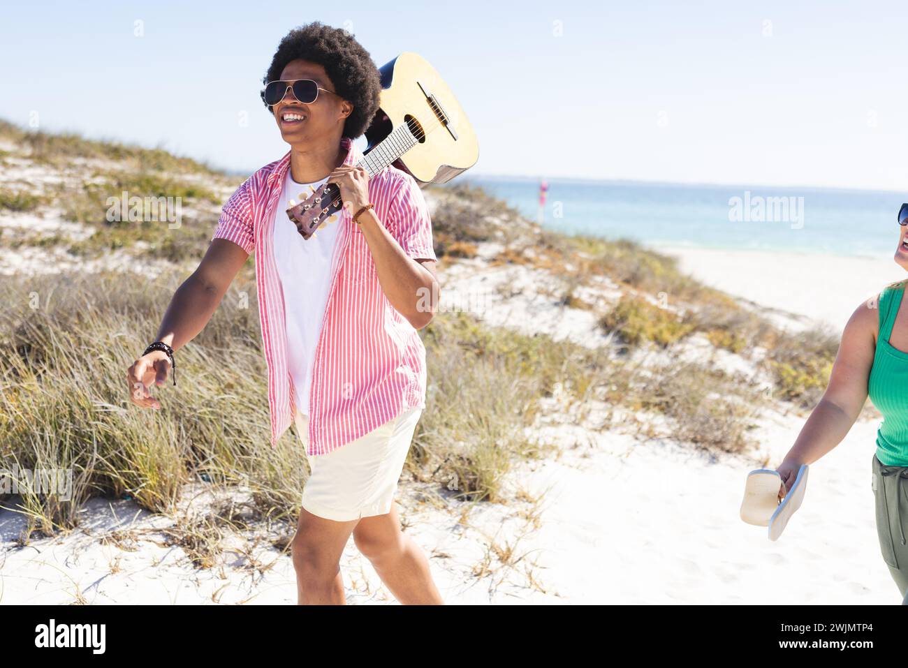 Junger afroamerikanischer Mann mit Gitarre genießt einen sonnigen Strandtag Stockfoto