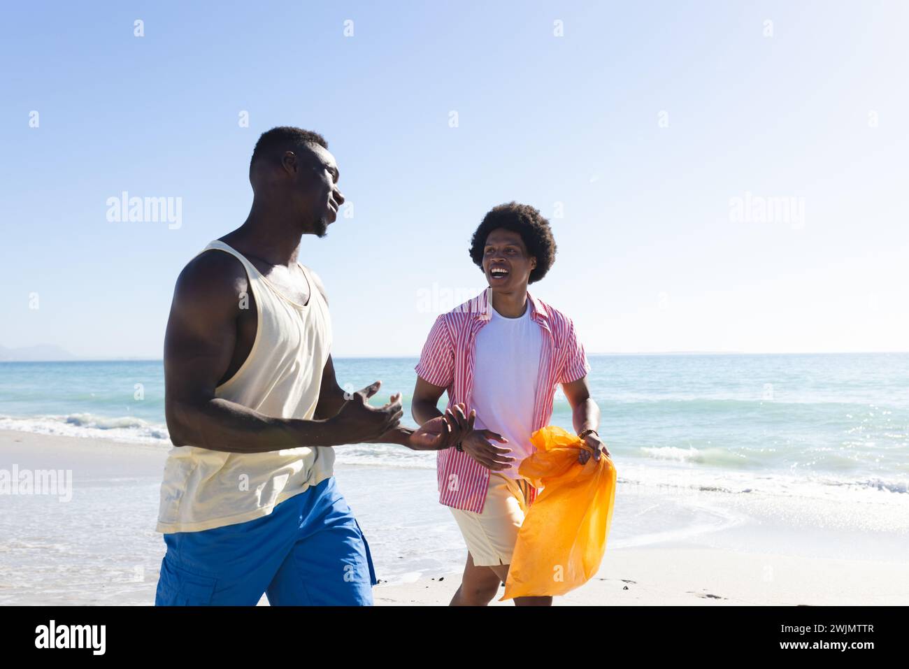 Ein afroamerikanisches Paar genießt einen sonnigen Strandtag und sammelt Müll Stockfoto