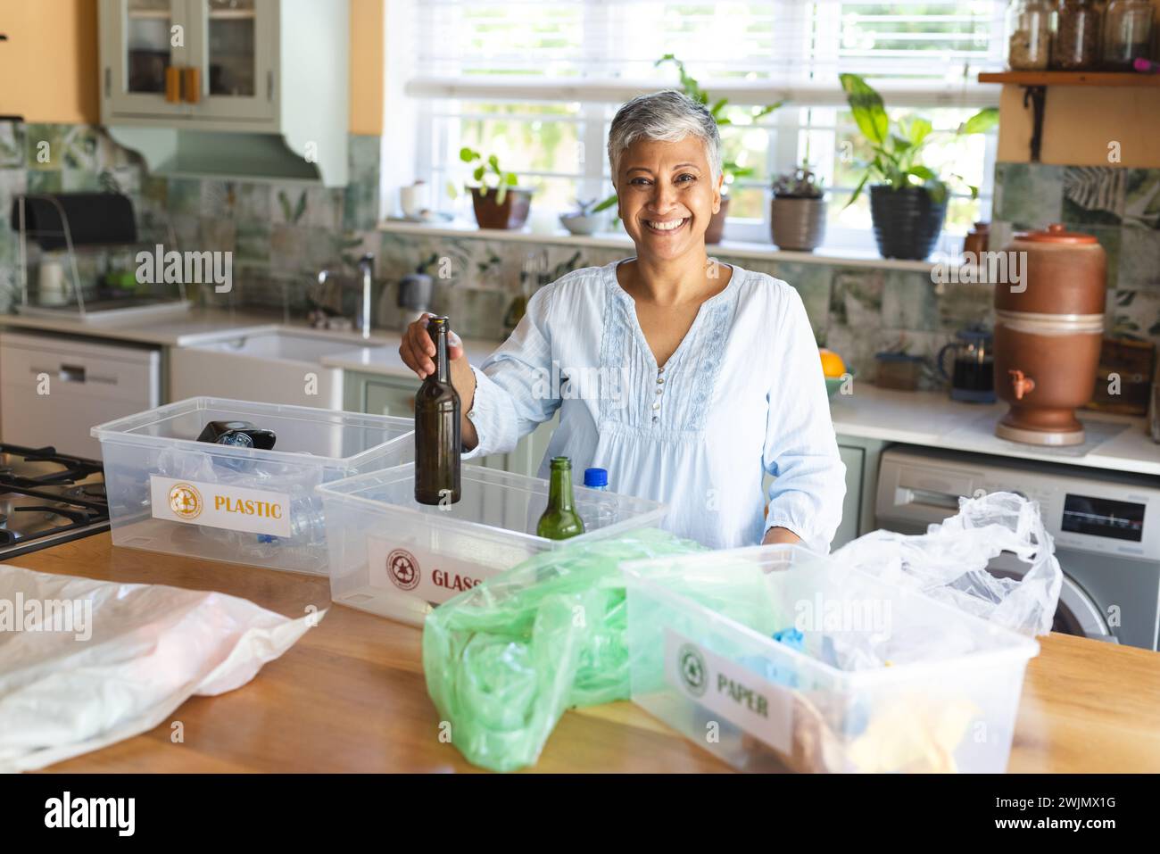 Eine reife Frau mit birassischer Rasse sortiert lächelnd zu Hause Recycling Stockfoto