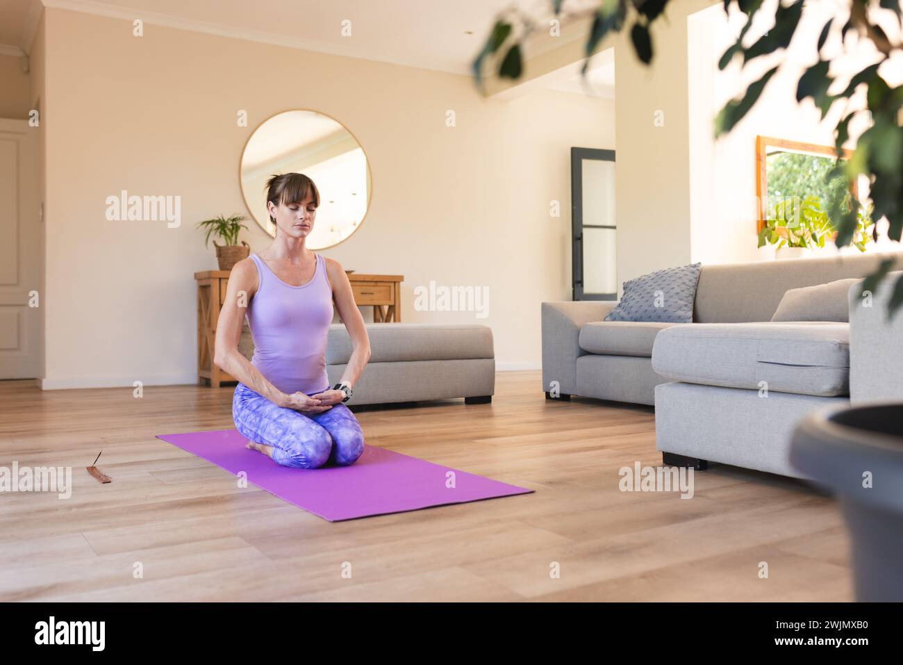 Eine Kaukasierin mittleren Alters übt Yoga in einem ruhigen Wohnzimmer mit Kopierraum Stockfoto