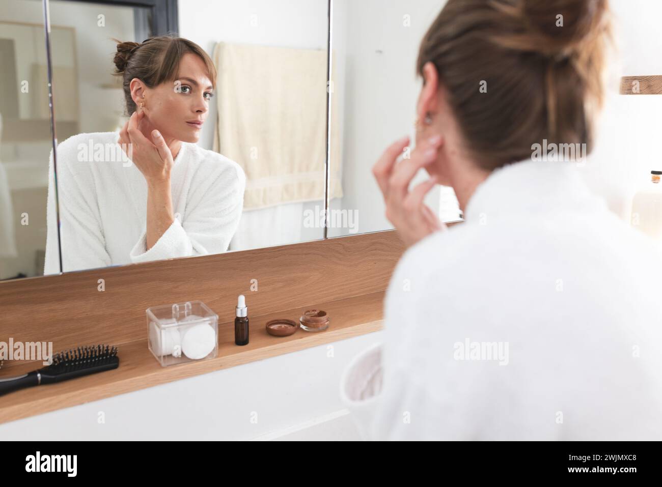 Eine kaukasische Frau mittleren Alters untersucht ihre Haut in einem Badezimmerspiegel Stockfoto