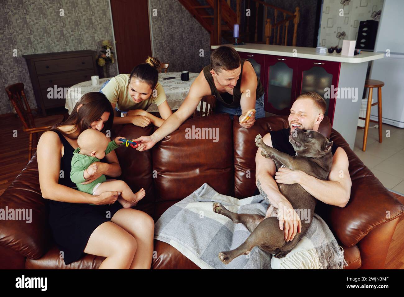 Ein junges verheiratetes Paar mit einem amerikanischen Tyrannehund sitzt auf dem Sofa im Wohnzimmer, während sie die jungen Eltern eines kleinen Mädchens besucht. Stockfoto