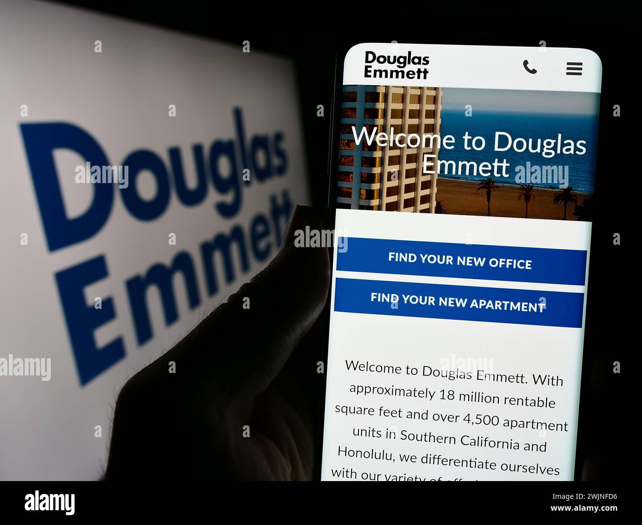Person, die ein Mobiltelefon hält, mit Webseite der US-Immobiliengesellschaft Douglas Emmett Inc. Vor dem Geschäftslogo. Konzentrieren Sie sich auf die Mitte des Telefondisplays. Stockfoto