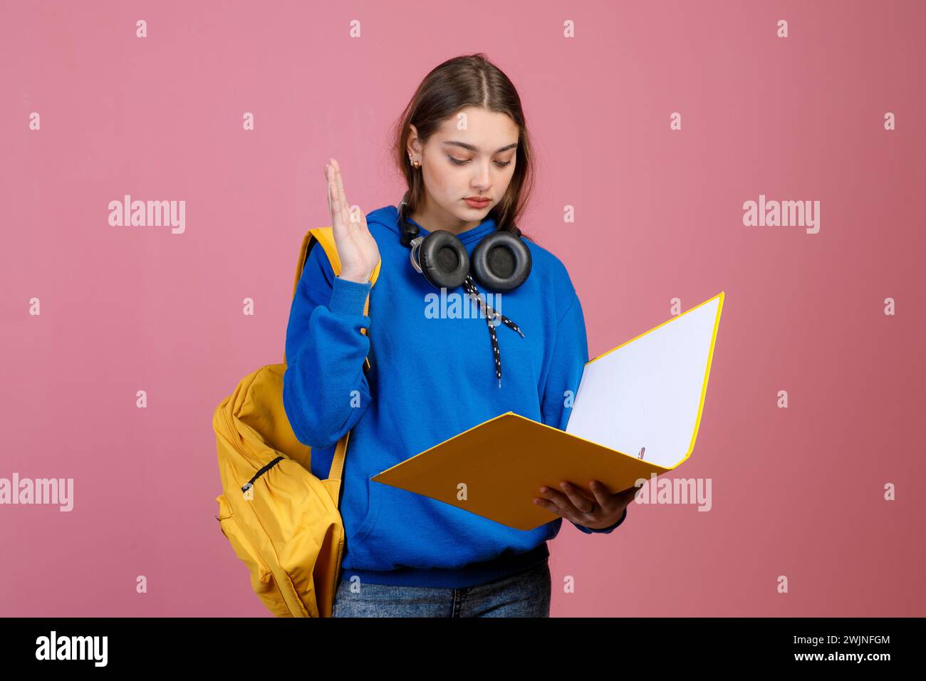 Hübsches Schulmädchen, das steht, liest, die Hand hebt, antwortet. Stockfoto