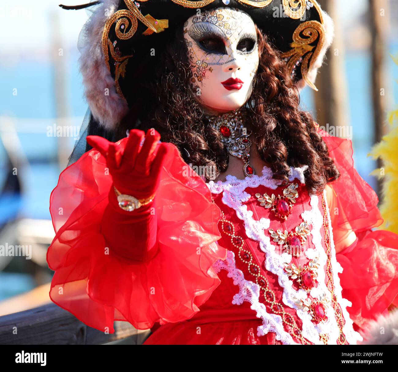 Venedig, VE, Italien - 13. Februar 2024: Elegante Frau in Maske mit Perücke und roten Handschuhen Stockfoto