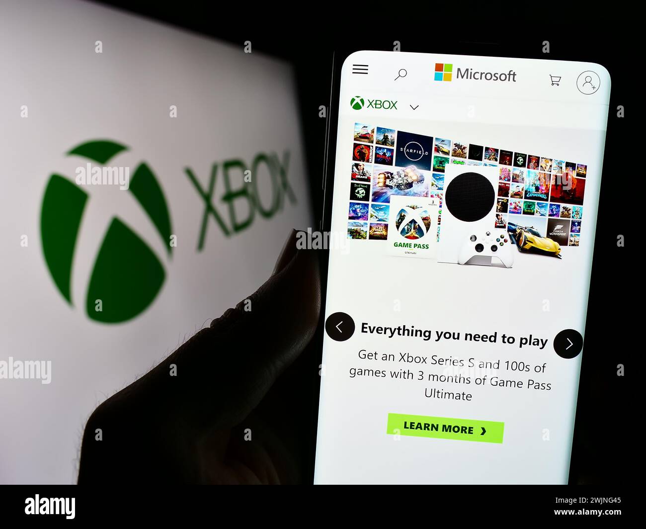 Person mit Smartphone und Website der Videospielkonsole Xbox (Microsoft) vor dem Firmenlogo. Konzentrieren Sie sich auf die Mitte des Telefondisplays. Stockfoto