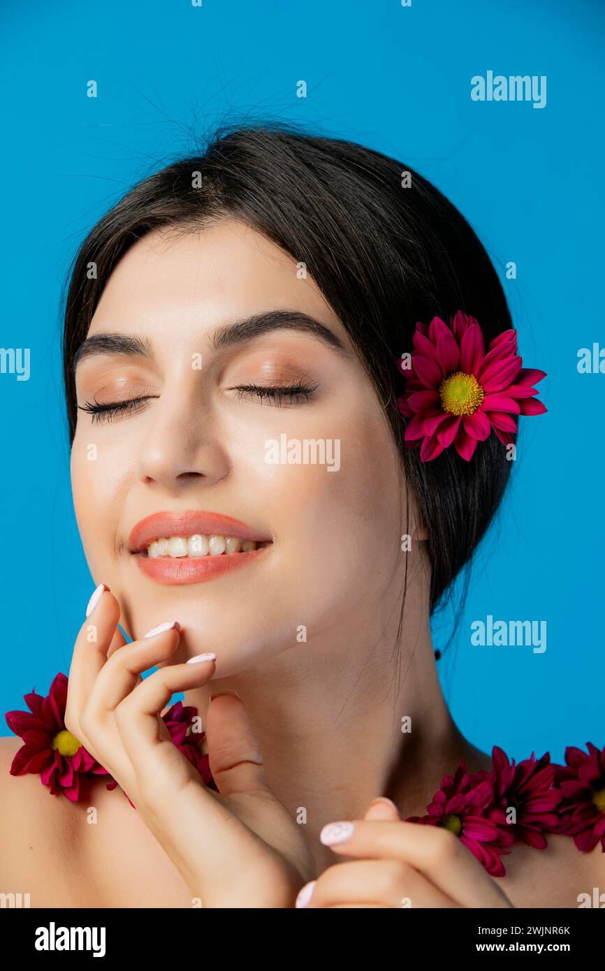 Elegantes, glückliches Model, das drinnen Fotoshooting macht, mit Blumen im Haar posiert und die Hände hebt. Stockfoto