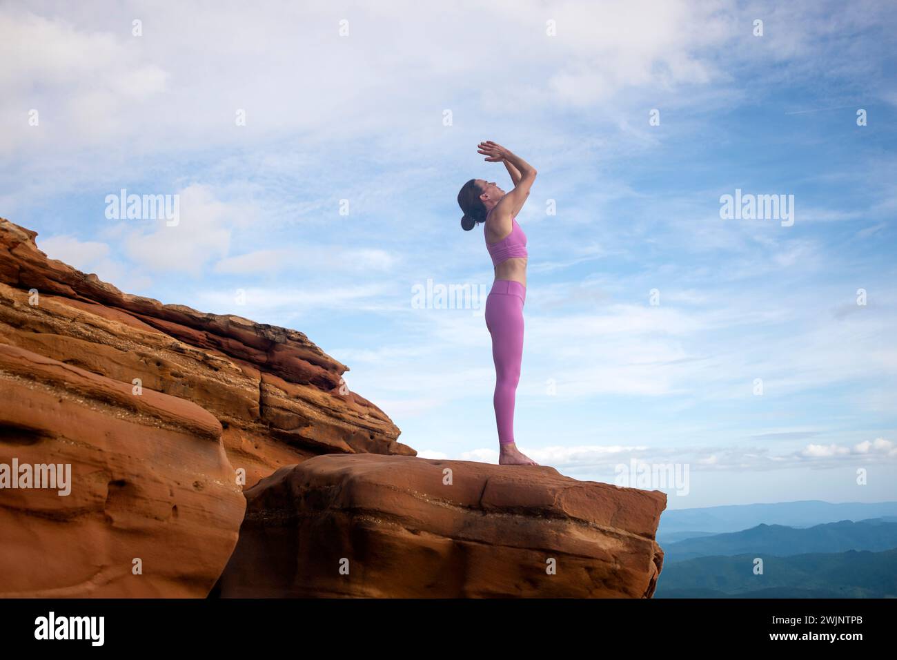 Eine sportliche Frau, die auf roten Felsen steht und meditiert. Stockfoto