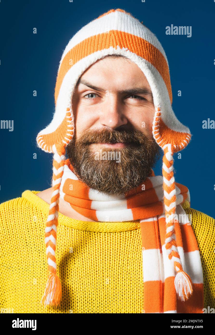 Nahaufnahme Porträt eines lächelnden bärtigen Mannes in gestreiftem Schal und Hut. Winteraccessoires. Hübscher Mann mit Bart und Schnurrbart in gelbem Pullover und lustig Stockfoto
