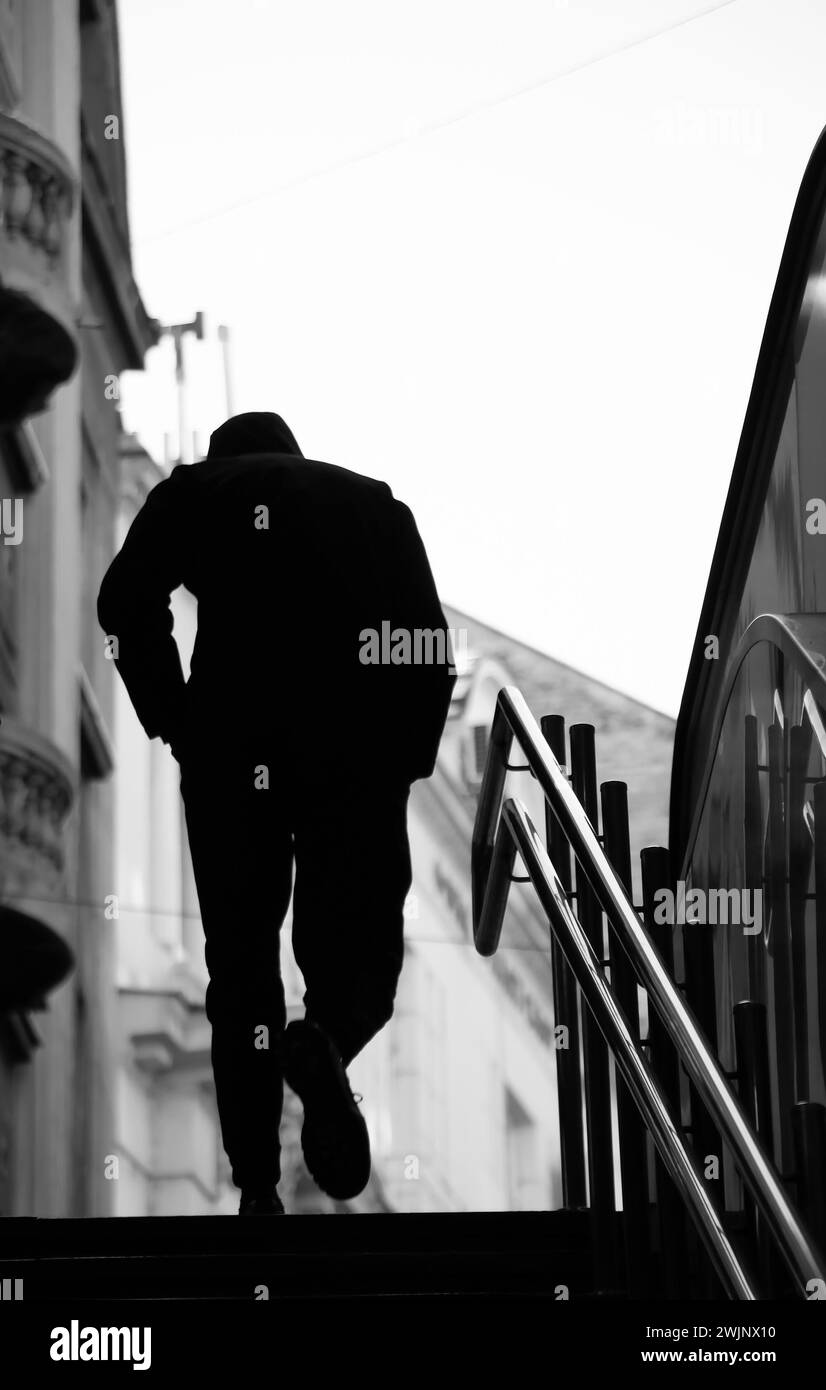 Verschwommene Silhouette eines jungen Mannes mit Händen in Taschen, der allein die U-Bahn-Treppe der Stadt mit glänzenden Geländern hinaufgeht Stockfoto
