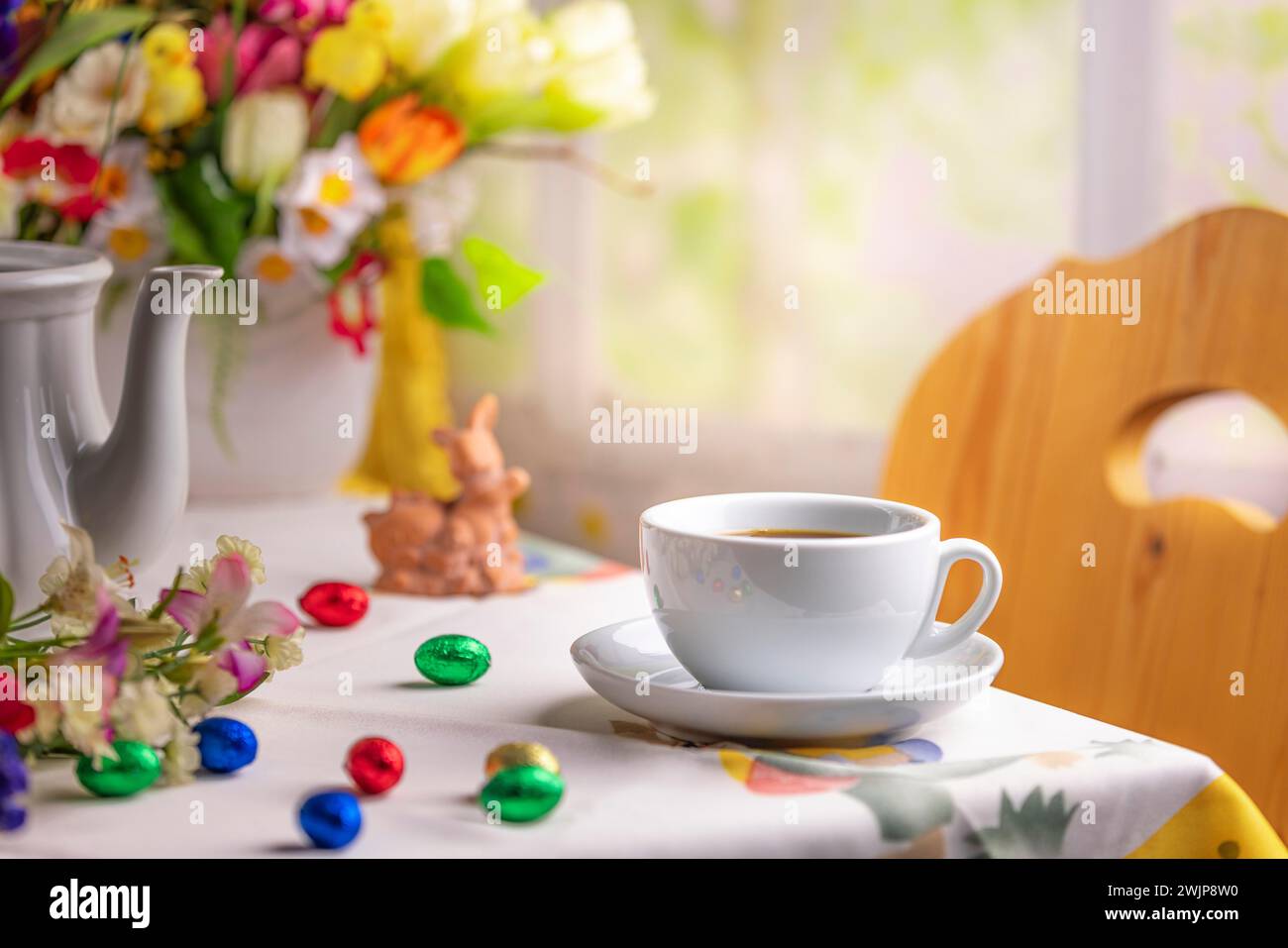 Eine Kaffeetasse auf einem Tisch mit Osterdekoration und einem bunten Blumenstrauß im Hintergrund Stockfoto
