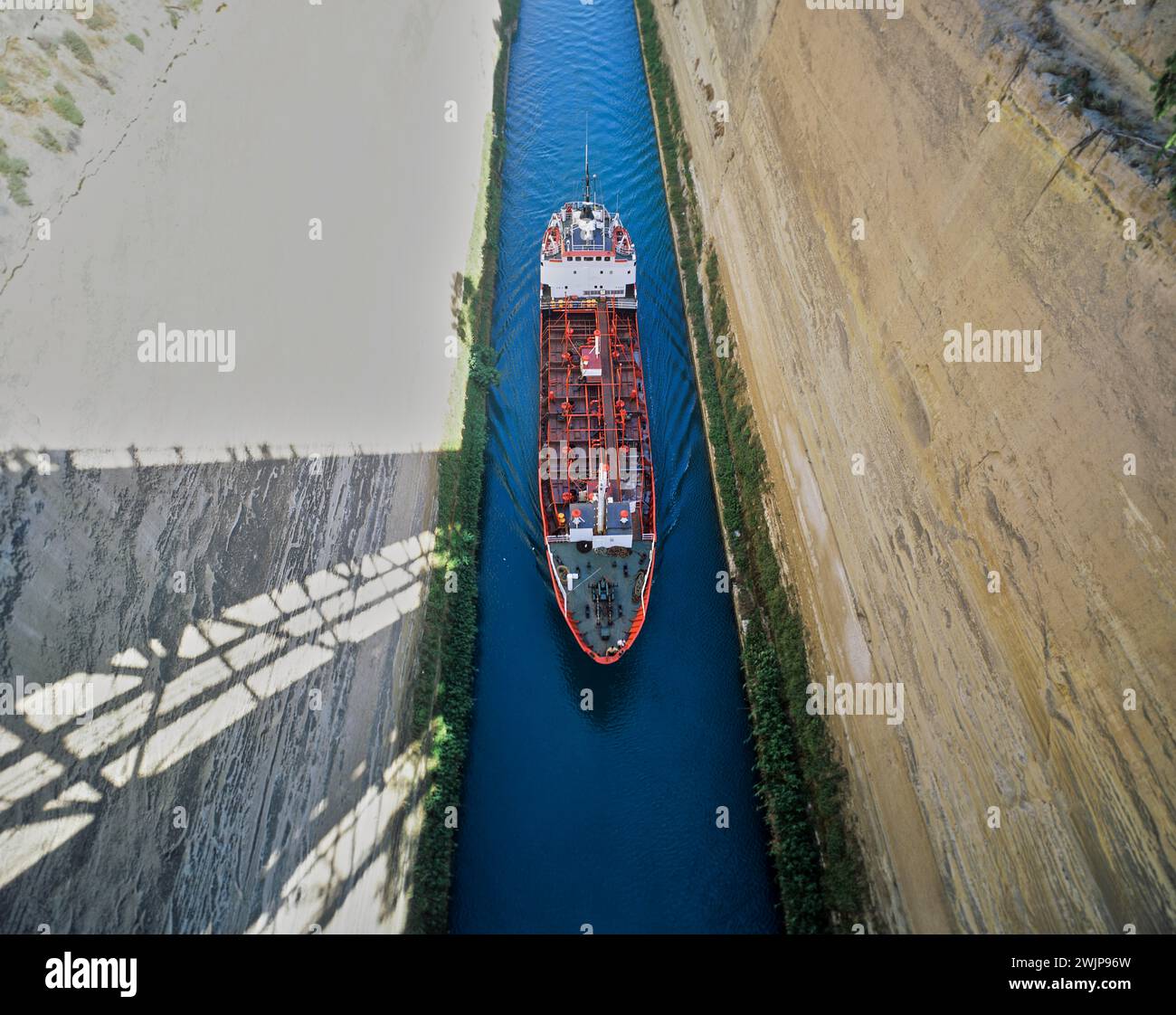 Aus der Vogelperspektive eines roten Schiffes, das durch einen schmalen Kanal unter einer Brücke fährt, Korinth Kanal, Korinth, Peloponnes, Griechenland Stockfoto