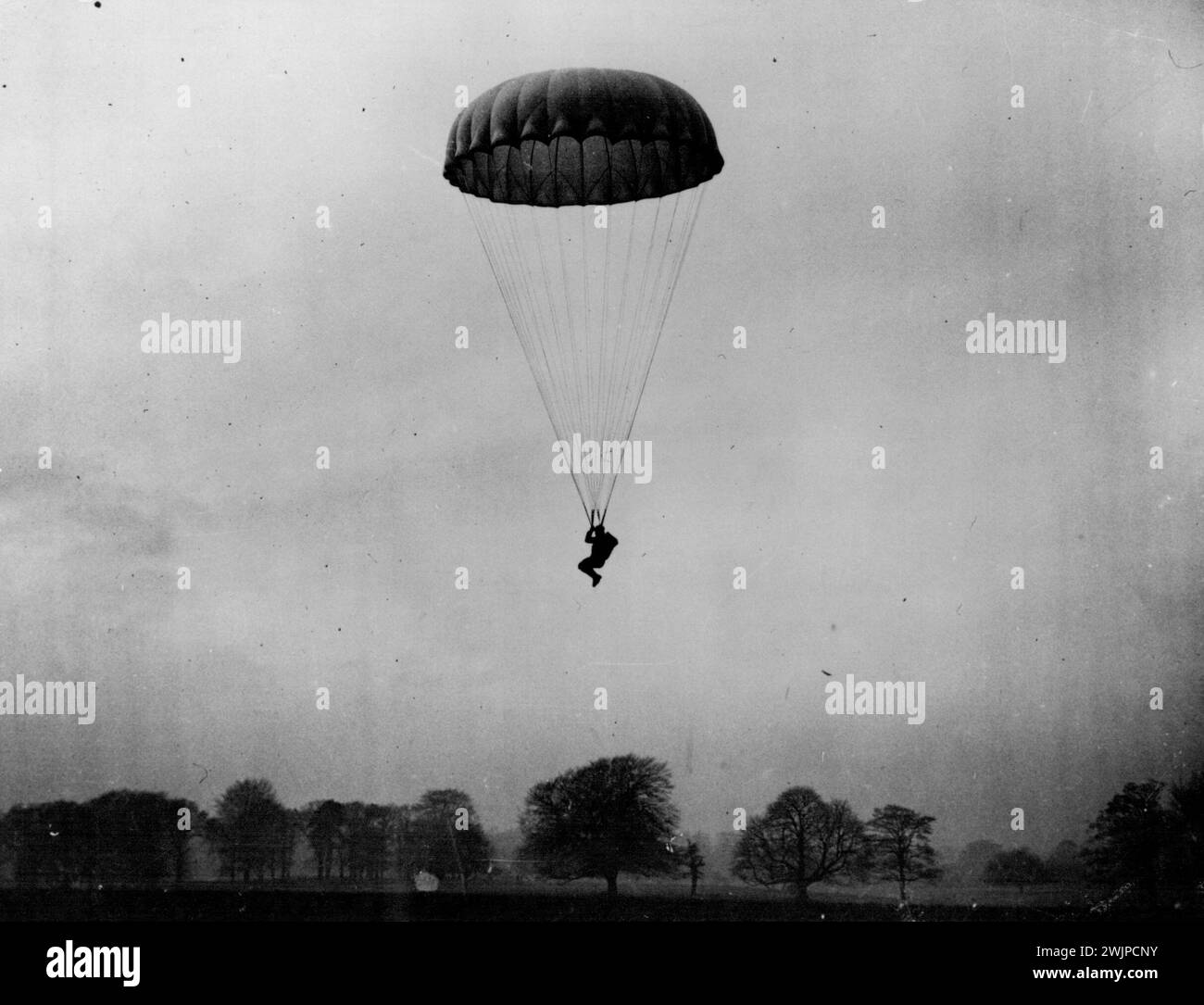 Diese Bilder von Fallschirmtruppen unter Anleitung wurden in einer geheimen R.A.F.-Station in Großbritannien erworben, wo Armee und Luftwaffe bei der Ausbildung zusammenarbeiten. Eine der Fallschirmtruppen landet kurz vor der Landung. Der Mann kontrolliert seine Landerichtung und hat seine Knie hochgehoben, bereit für den Schock der Landung. Juli 1955 Stockfoto