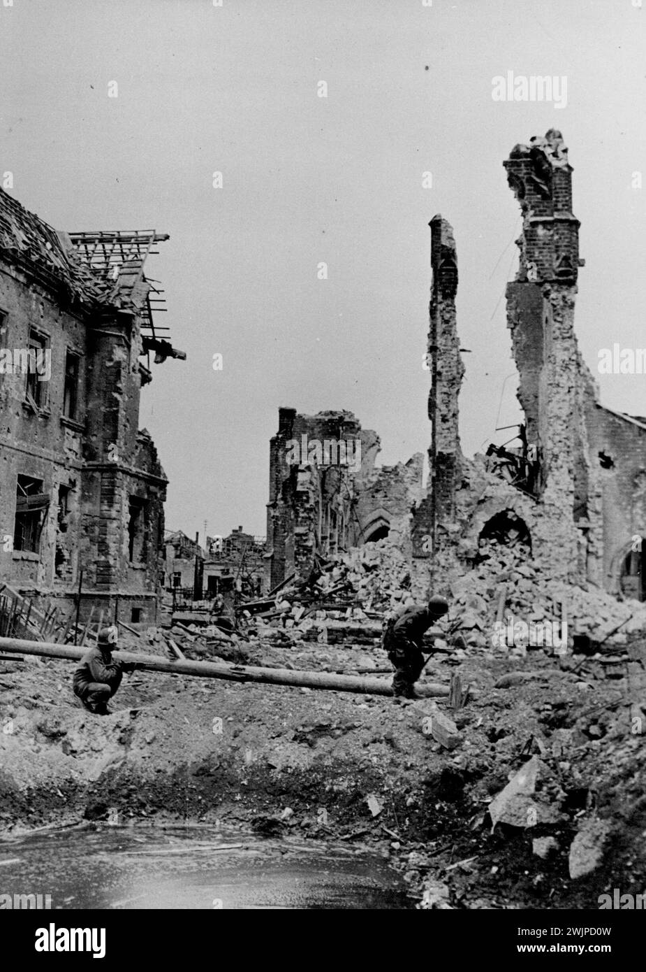 US-Soldaten patrouillieren Fraulautern -- zwei Infanteristen der 65. Division, der 3. US-Armee, marschieren am 20. März 1945 an einem wassergefüllten Bombenkrater in Fraulautern vorbei, als sie die Stadt für Nazi-Nachzügler patrouillieren. Eine zerstörte Kirche ist im Hintergrund. Fraulautorn liegt 16 Meilen nordwestlich von Saarbarucken. Januar 1945. (Foto: U.S. Signal Corps Photo). Stockfoto