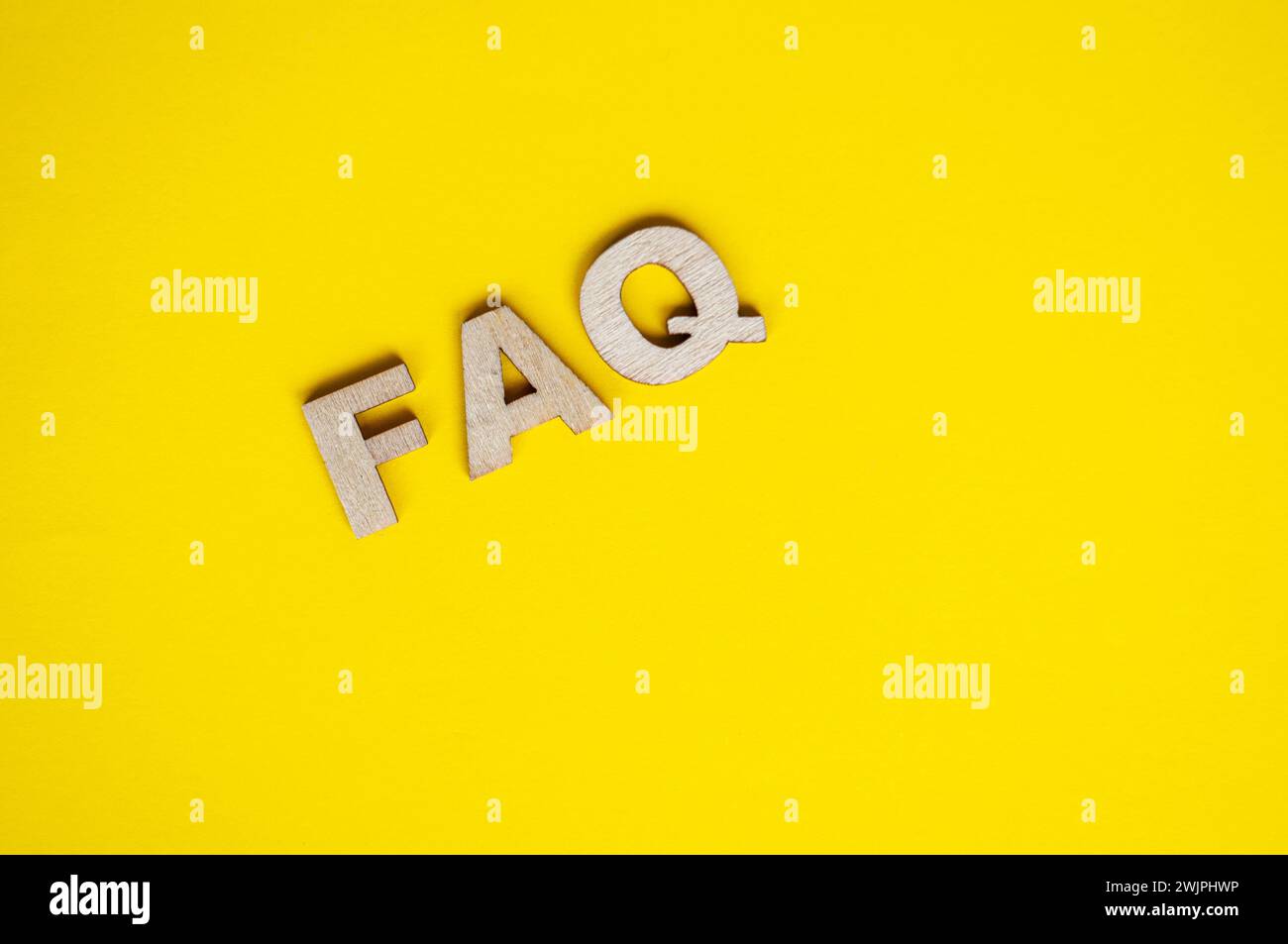 Draufsicht des hölzernen FAQ-Textes auf gelbem Hintergrund. Konzept häufig gestellte Fragen. Stockfoto
