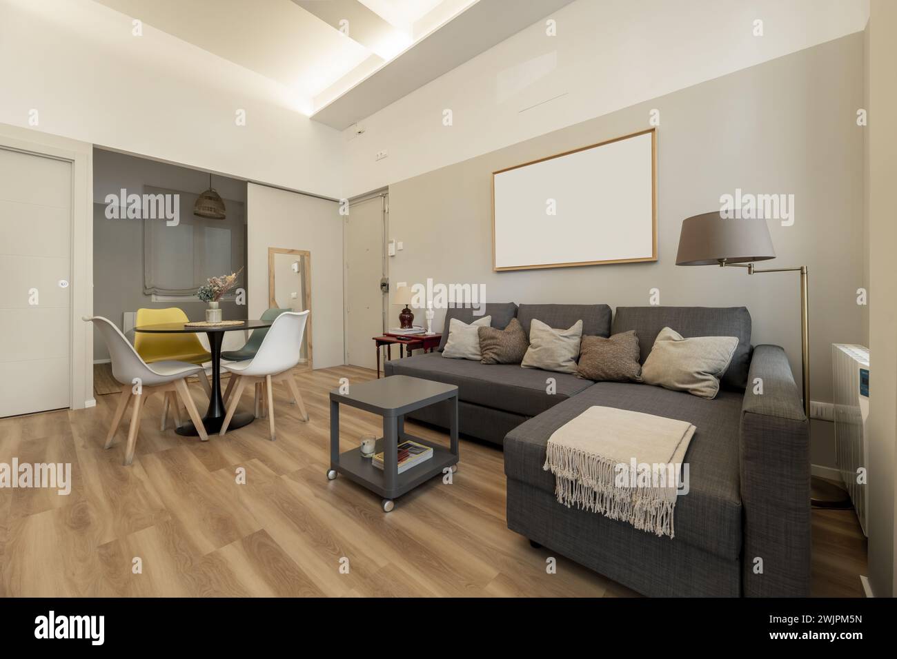 Wohnzimmer eines kleinen Wohnhauses im Loft-Stil mit Sofa mit Chaiselonge mit dunkelgrauen Stoffen, runden Esszimmermaße und hellem Parkett Stockfoto