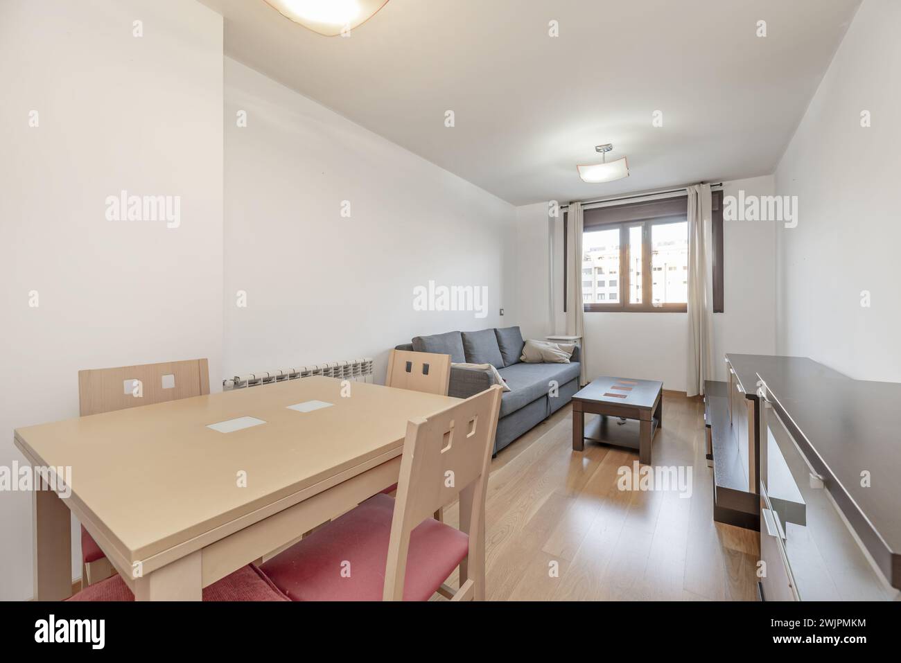 Kleines Wohnzimmer in einem Haus mit hellen Holzmöbeln mit dunklen Arbeitsflächen, einem buchenfarbenen Esstisch aus Holz mit passenden Stühlen und einem grauen Fabr Stockfoto