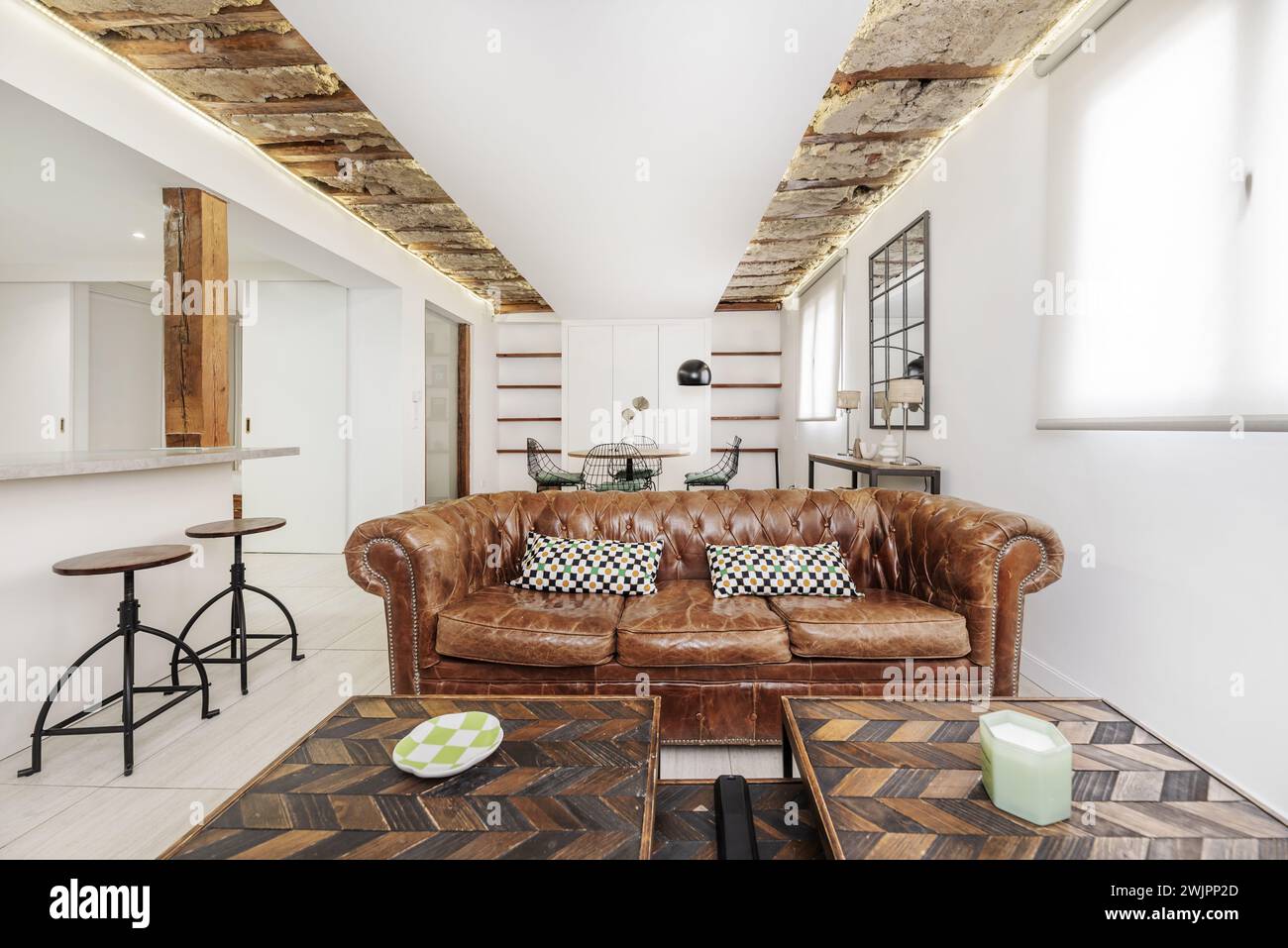 Ein Wohnzimmer mit moderner Einrichtung im industriellen Stil mit chesterfield-Ledersofa und Holzbalken an der Decke Stockfoto