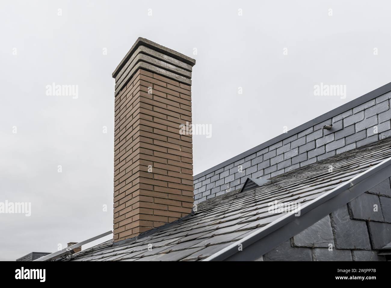 Gemauerter Kamin auf dem Dach eines Hauses mit schwarzen Schieferziegeln Stockfoto