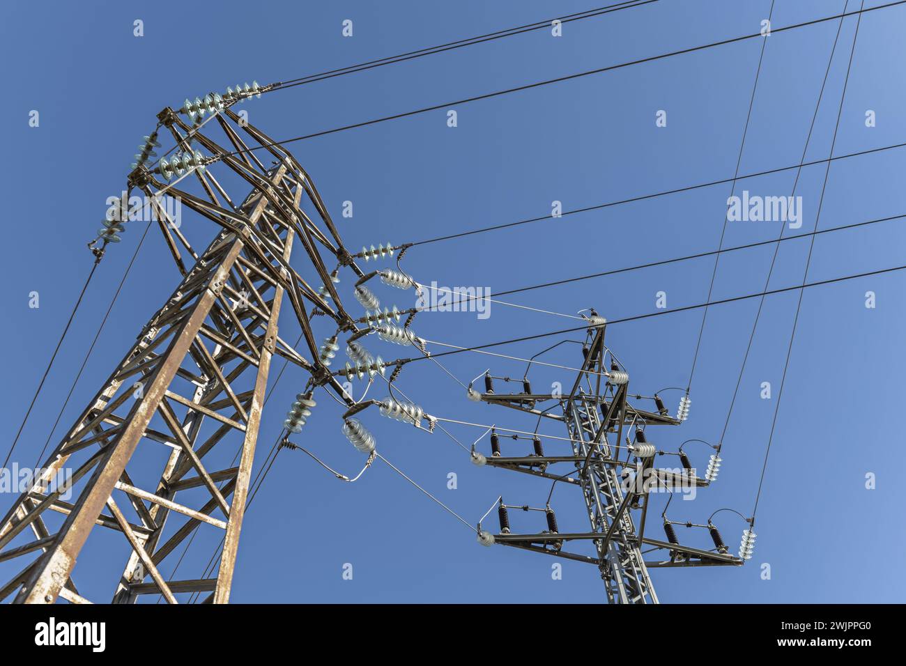 Einige Hochspannungstürme, die an einem schönen Tag mit klarem Himmel Strom durch ihre Kabel mit Glockenisolierungen transportieren Stockfoto